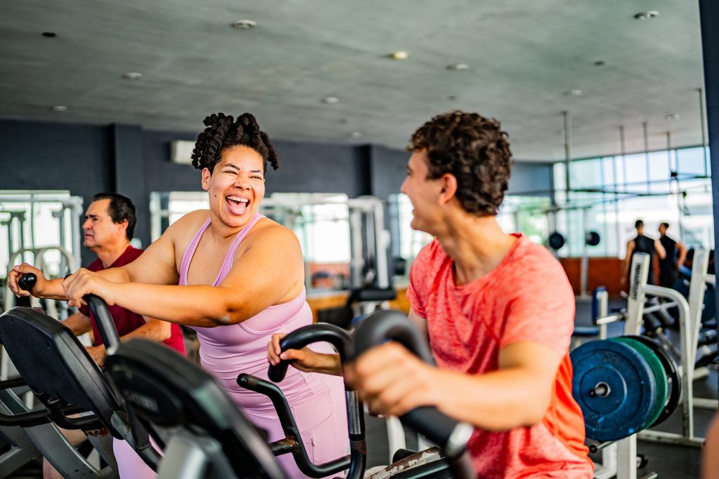 Friends talking while exercising on elliptical cross trainer at gym 